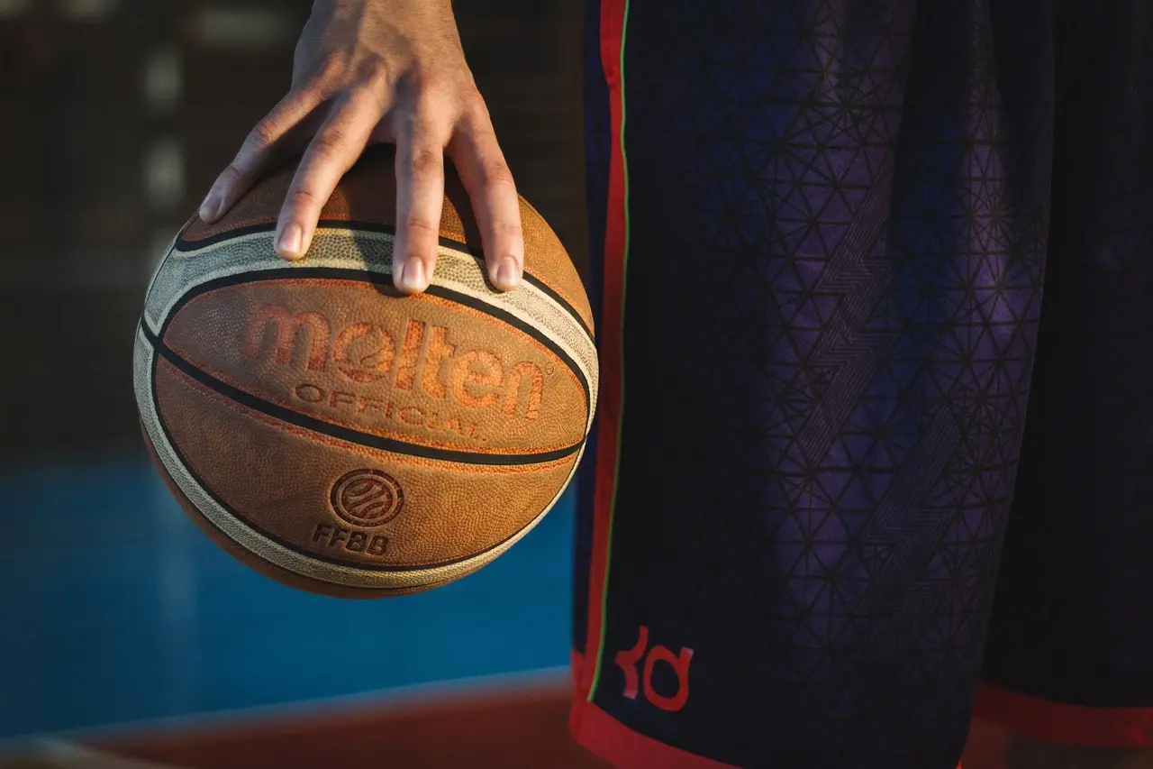 Hånd der holder en basketball ved siden af en spiller i basketballshorts