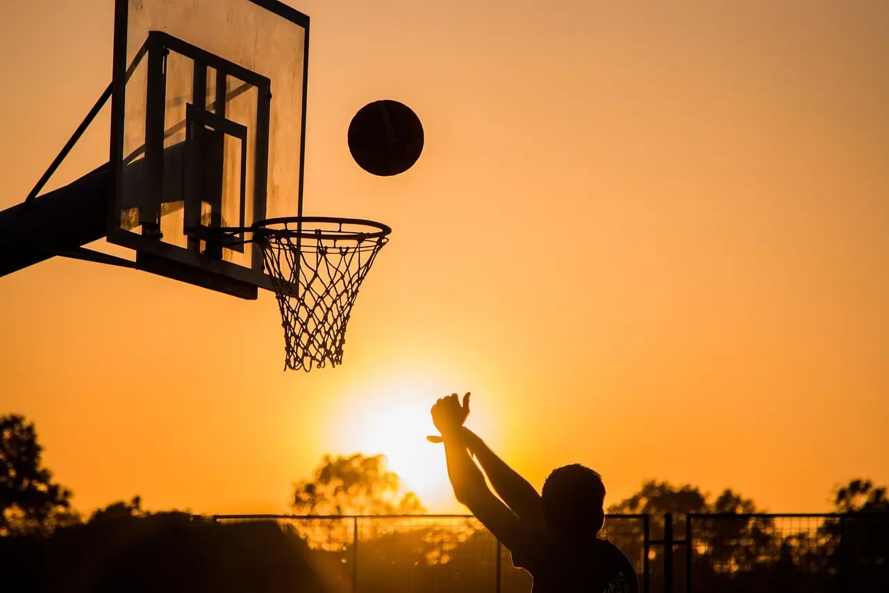 Silhuet af en basketballspiller der skyder mod en kurv i solnedgang