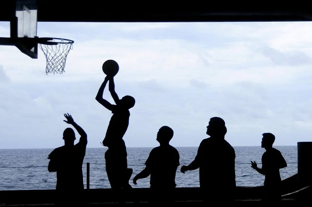 Silhuetter af personer der spiller basketball ved en kurv med havet i baggrunden