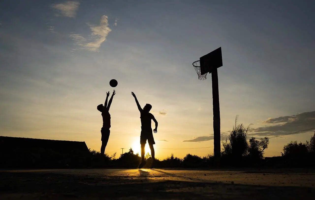 To personer der spiller basketball ved en kurv i solnedgang